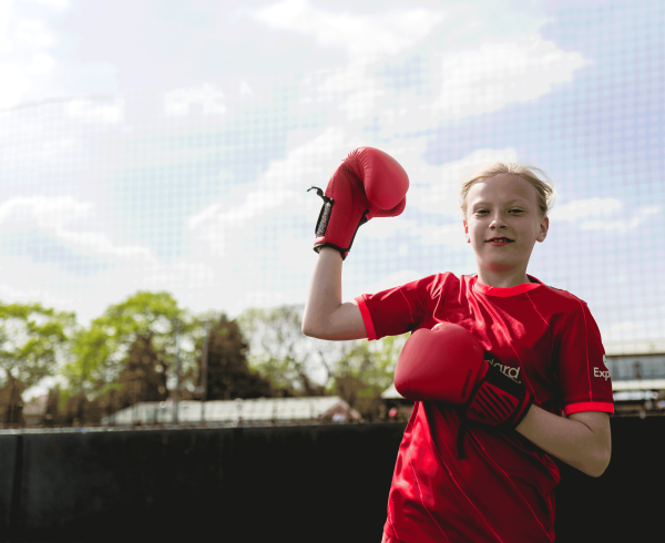 A young girl wearing boxing gloves pumping her fist into the air