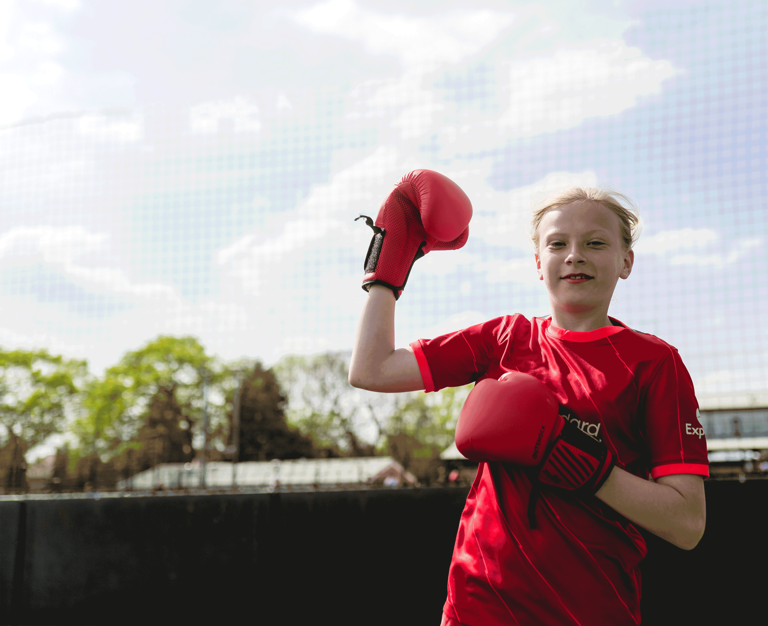 A young girl wearing boxing gloves pumping her fist into the air
