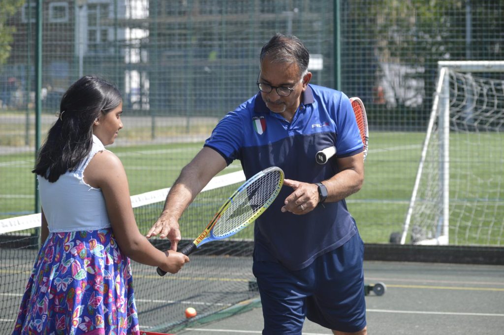 A young girl and her coach on a tennis court looking at a tennis racquet.